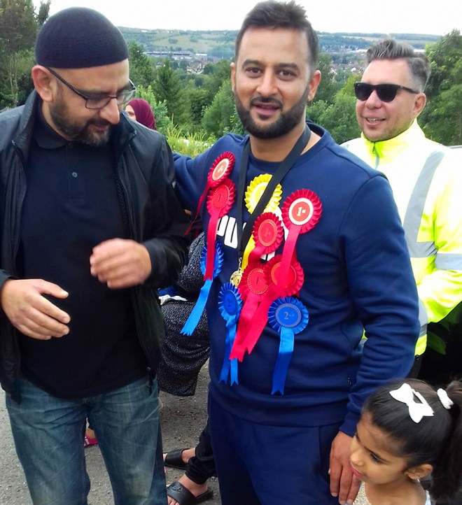 Newbie plot-holder gazes longingly (“next year that will be me”) at the rosette covered chest of the ‘Plot Holder of the Year’ winner. Winner not taking any chances – has hired bodyguard to protect against any snatch and grab attempts on the prizes.